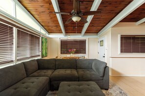 A living room with a sectional sofa, a ceiling fan, and a window with blinds.