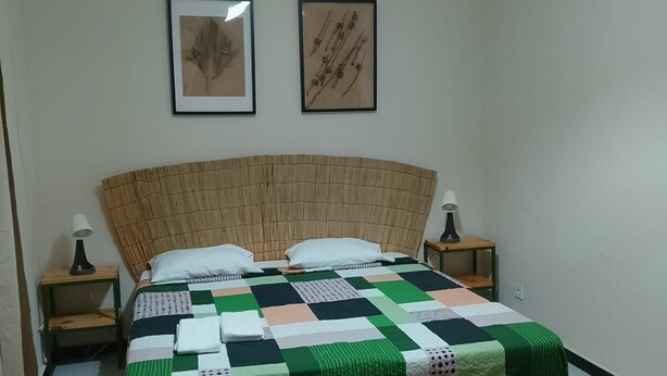Un lit bien fait, recouvert d’une couvre-lit à carreaux, deux tableaux encadrés accrochés au mur et une lampe de chevet de chaque côté.