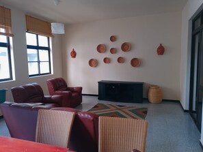 Ein Wohnzimmer mit einer Couch, Sesseln, einem Fernseher und dekorativen Tellern an der Wand.