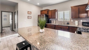 A kitchen with granite countertops, wooden cabinets, a stainless steel refrigerator, and a black stove. - Modern 2BR/2BA Home • King Bed • Smart TVs (D) (El Paso)