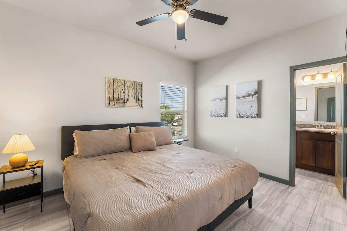 A bedroom with a bed, a nightstand, a lamp, a ceiling fan, and artwork on the walls.