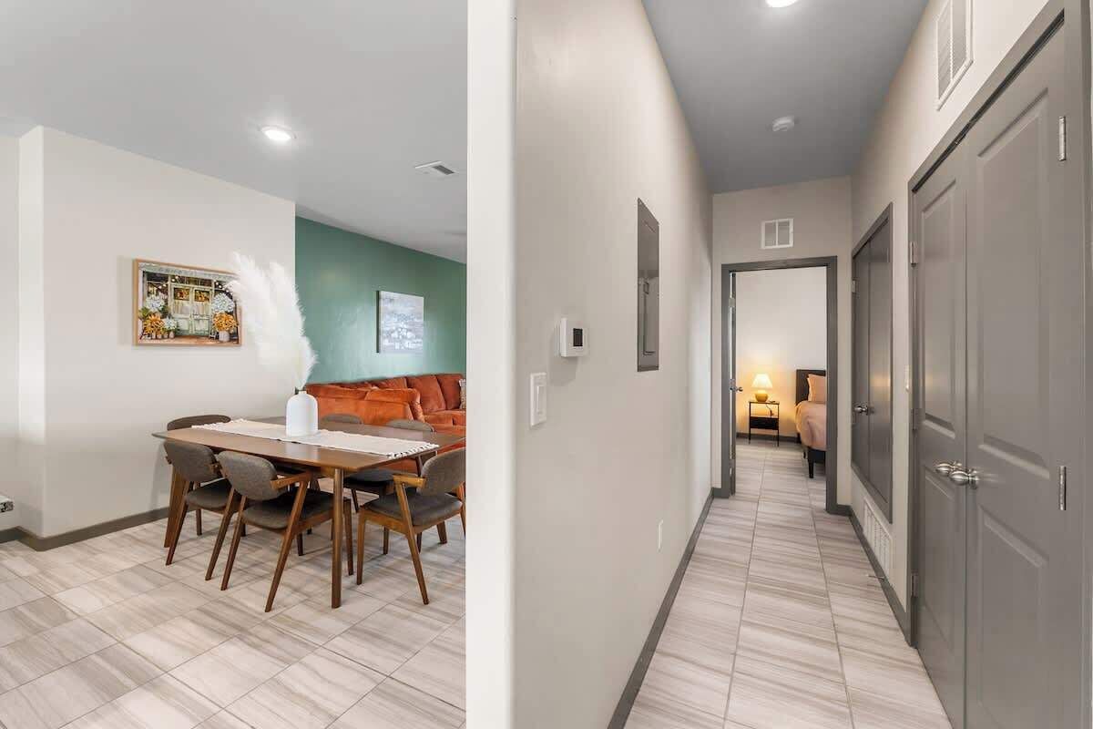 A hallway with a dining area on the left, featuring a table and chairs, and a bedroom with a bed and nightstand on the right.