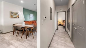 A hallway with a dining area on the left, featuring a table and chairs, and a bedroom with a bed and nightstand on the right. - Modern 2BR/2BA Home • King Bed • Smart TVs (D) (El Paso)
