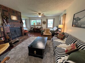 A cozy living room with a fireplace, a sofa, a coffee table, and a ceiling fan.