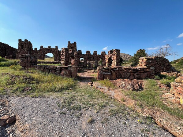 Antiche rovine in pietra con archi e mura, contrassegnate con la scritta 'Corte di Erode', immerse in un prato erboso sotto un cielo sereno.