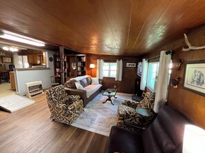 A cozy living room with a brown leather sofa, patterned armchairs, a small table, and a bookshelf.