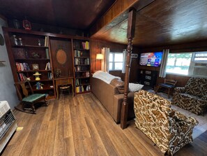 A cozy living room with a wooden floor, a brown sofa, a patterned armchair, a rocking chair, and a bookshelf filled with books and decorative items. - Private Ranch Retreat with Panoramic Views of the Wichita Mountains (Roosevelt)
