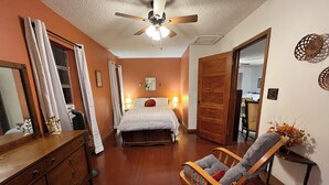 Une chambre à coucher avec un lit en bois, une table de chevet, une commode, une chaise et un ventilateur de plafond.