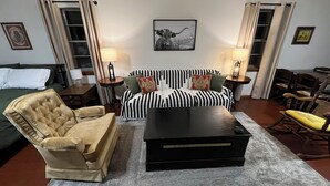 Une pièce comprenant un canapé, un fauteuil et une table basse. Deux lampes sont posées sur des tables d’appoint.
