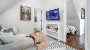 A modern loft apartment with a high ceiling, a loft bed, a sofa, a coffee table, and a TV mounted on the wall. - The Loft at Marble Place: Cozy Family Retreat (Courtenay)