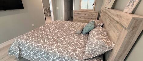 Een slaapkamer met een groot bed, een dressoir en een aan de muur bevestigde televisie.