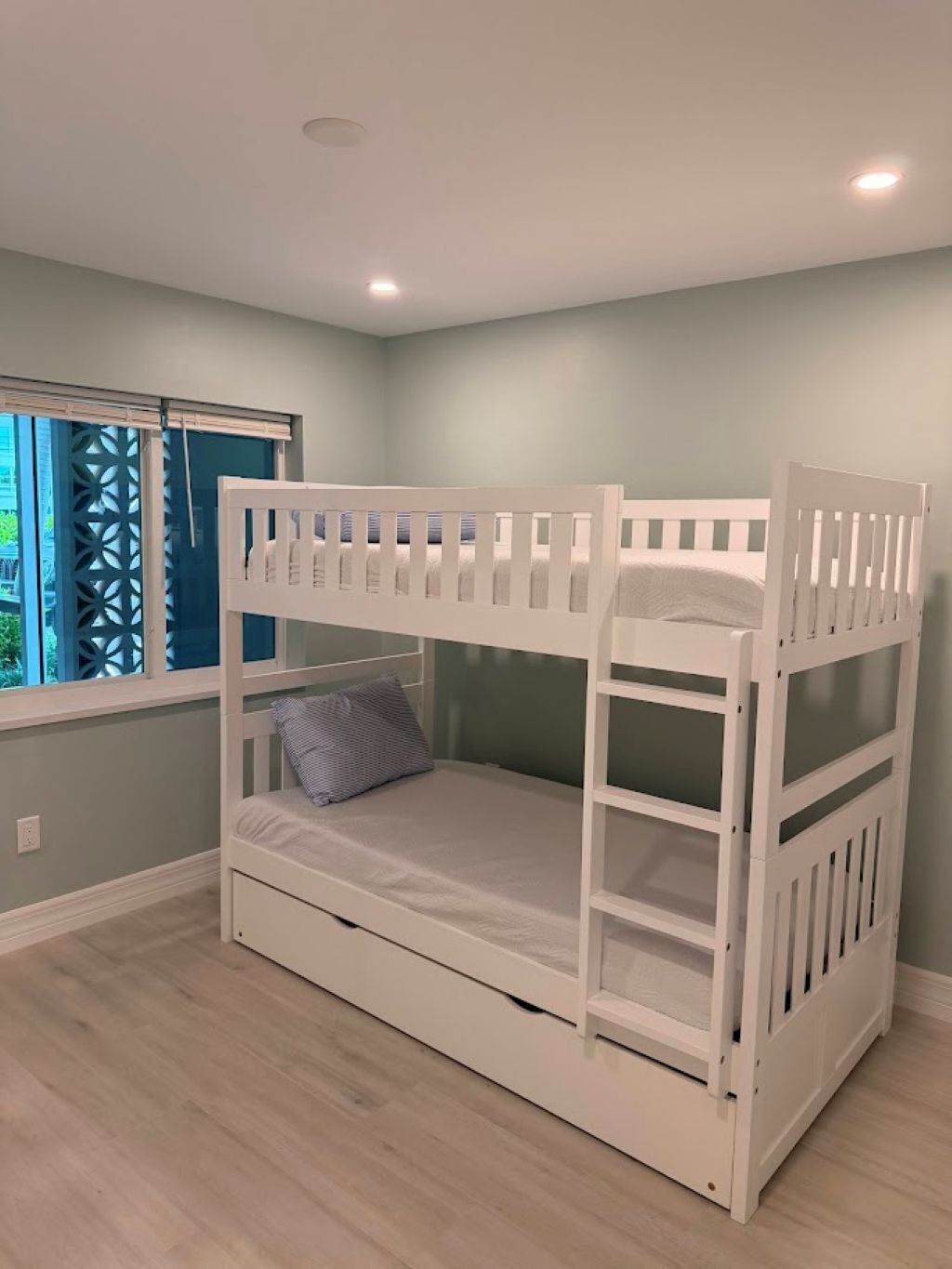 Una cama litera en una habitación con paredes azul claro y una ventana con persianas.