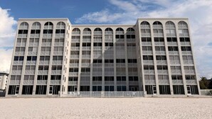 Een modern gebouw met een symmetrische gevel, grote ramen en een plat dak, gelegen in een zandrijk gebied onder een heldere lucht.
