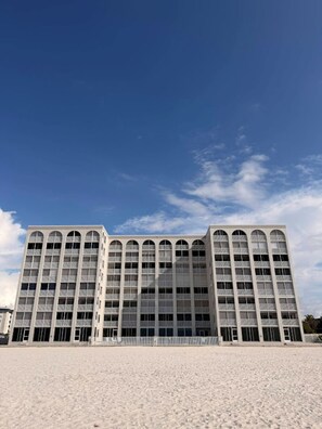 Ein modernes Gebäude mit einer symmetrischen Fassade, großen Fenstern und einem flachen Dach, gelegen in einer sandigen Umgebung unter wolkenlosem Himmel.