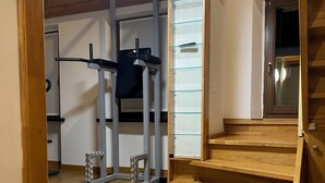 A wooden staircase leading to a second floor, a pull-up bar, and a wall-mounted shelf with glass doors.