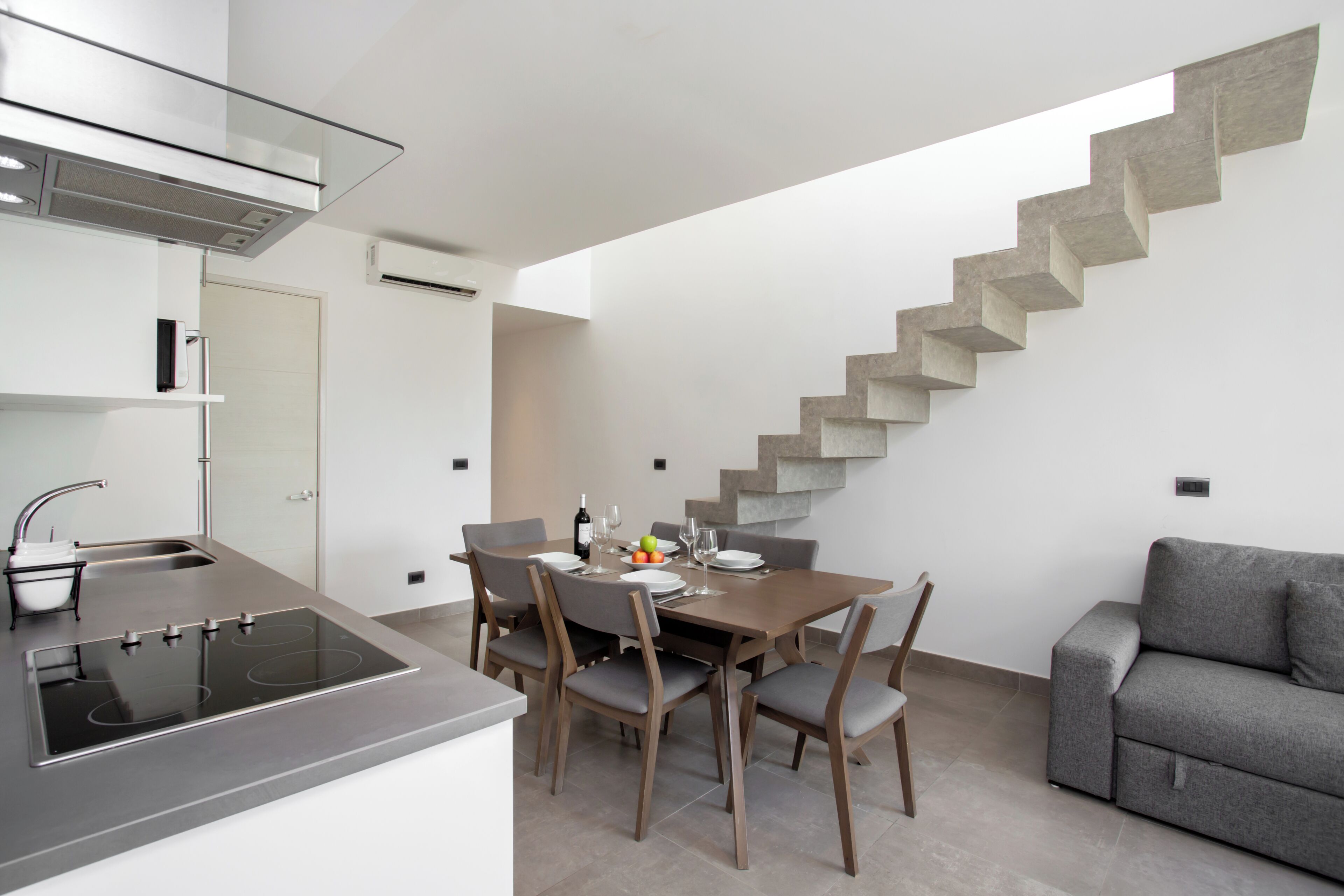 A modern kitchen with a built-in stove, dining table, and chairs. A staircase leads to an upper level.