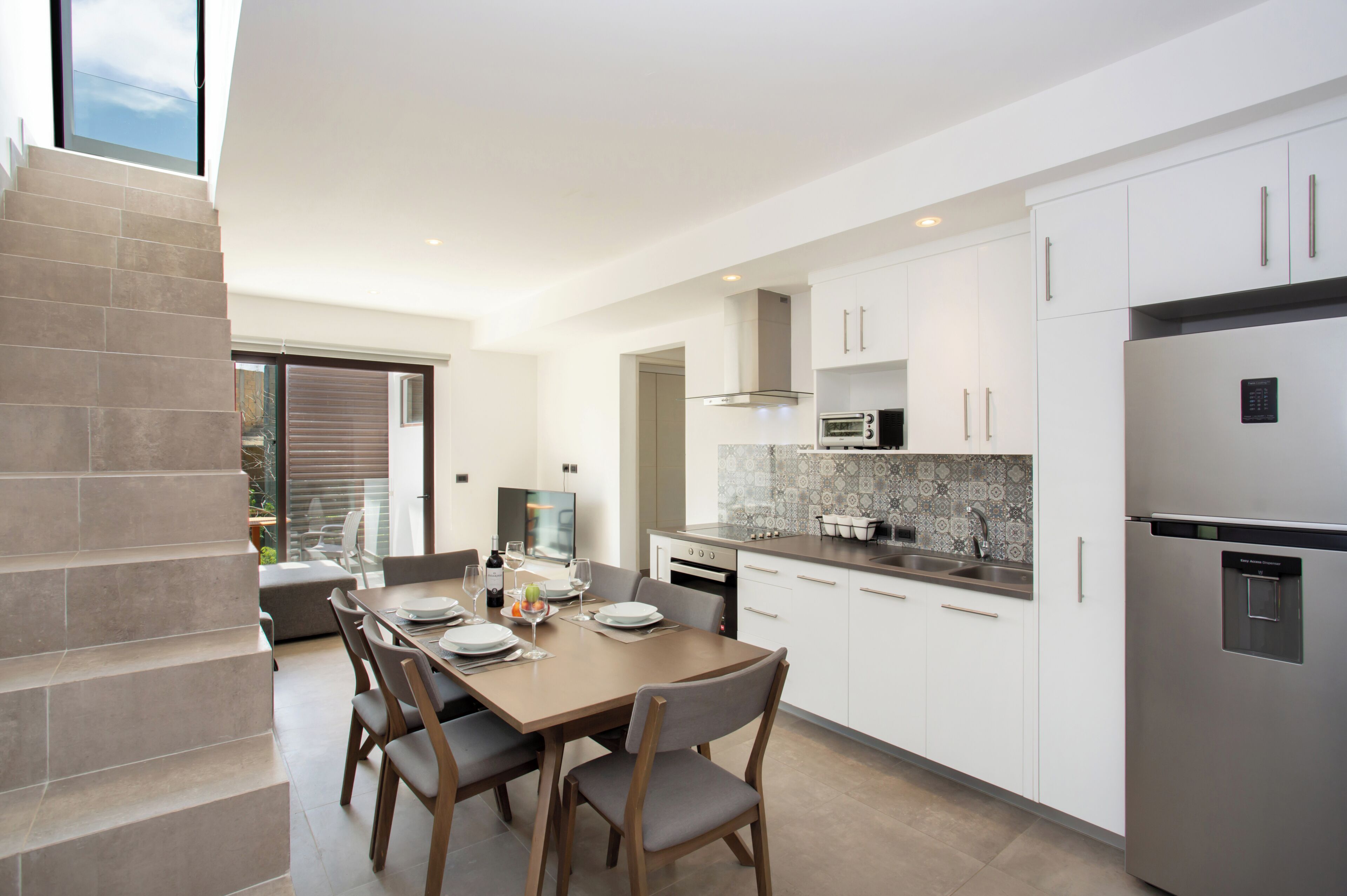 A modern kitchen with white cabinets, stainless steel appliances, and a dining area with a wooden table and chairs.