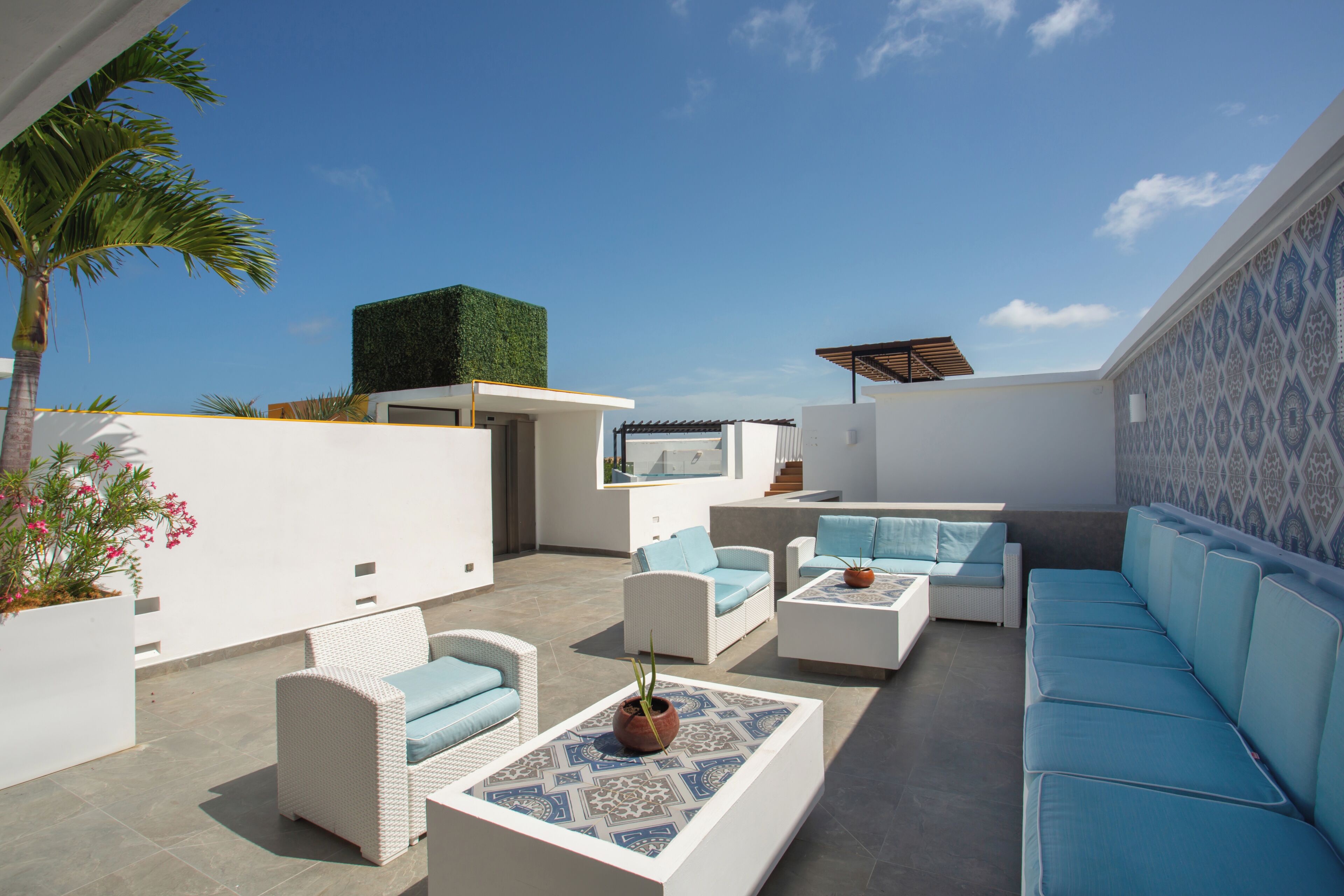 Un espace extérieur moderne, aménagé avec des meubles blancs et bleus, un mur végétal et un mur orné de motifs.