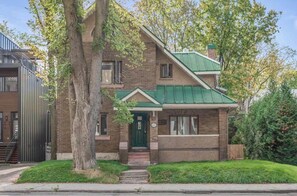 A two-story house with a green roof, brick walls, and a front porch.