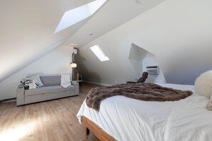 A modern loft bedroom with a sloped ceiling, a large bed, a sofa, and a skylight. - Adorable 1-bedroom apartment with AC in charming Québec (Québec)