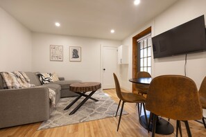 A living room with a grey sofa, a round coffee table, and a dining area with a table and chairs. - Adorable 1-bedroom apartment with AC in charming Québec (Québec)