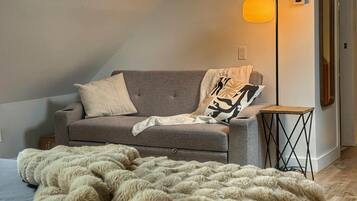 A cozy room with a grey sofa, a fluffy beige blanket, and a modern floor lamp.