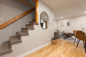 A staircase with carpeted steps and wooden handrails, a round mirror, a gray sofa, a coffee table, and a wicker basket on a wooden floor. - Adorable 1-bedroom apartment with AC in charming Québec (Québec)