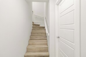 A staircase with a handrail, white walls, and a door.