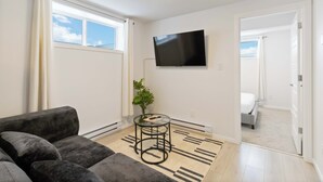 Ein modernes Wohnzimmer mit einer Couch, einem kleinen runden Tisch mit Pflanze, einem Flachbildfernseher und einem gemusterten Teppich.