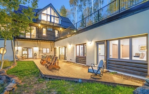 A two-story log cabin with a deck, outdoor seating, and a large window overlooking the yard. - NEW! Luxury Family & Group Retreat | Hot Tub, Gym + Mountain Views | Sleeps 14 (Telluride)