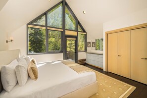 Ein Schlafzimmer mit großem Fenster, einem Bett mit Kissen, einem Schminktisch und einem Kleiderschrank.