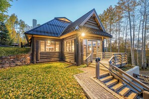 Une cabane en rondins avec une entrée en verre, un mur en pierre et une terrasse en bois.