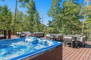 Un bain à remous sur une terrasse en bois, avec des meubles d’extérieur et une vue sur les arbres.
