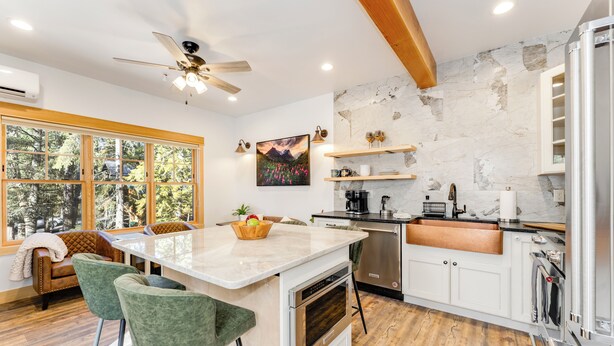 A modern kitchen with a large island, bar stools, a ceiling fan, and a stone accent wall.