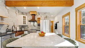 A modern kitchen with a marble countertop, wooden ceiling beams, and a central island with a fruit bowl.