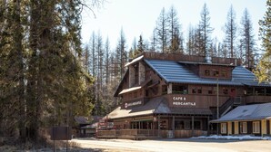 A rustic building with a cafe and mercantile on the ground floor, surrounded by tall trees.