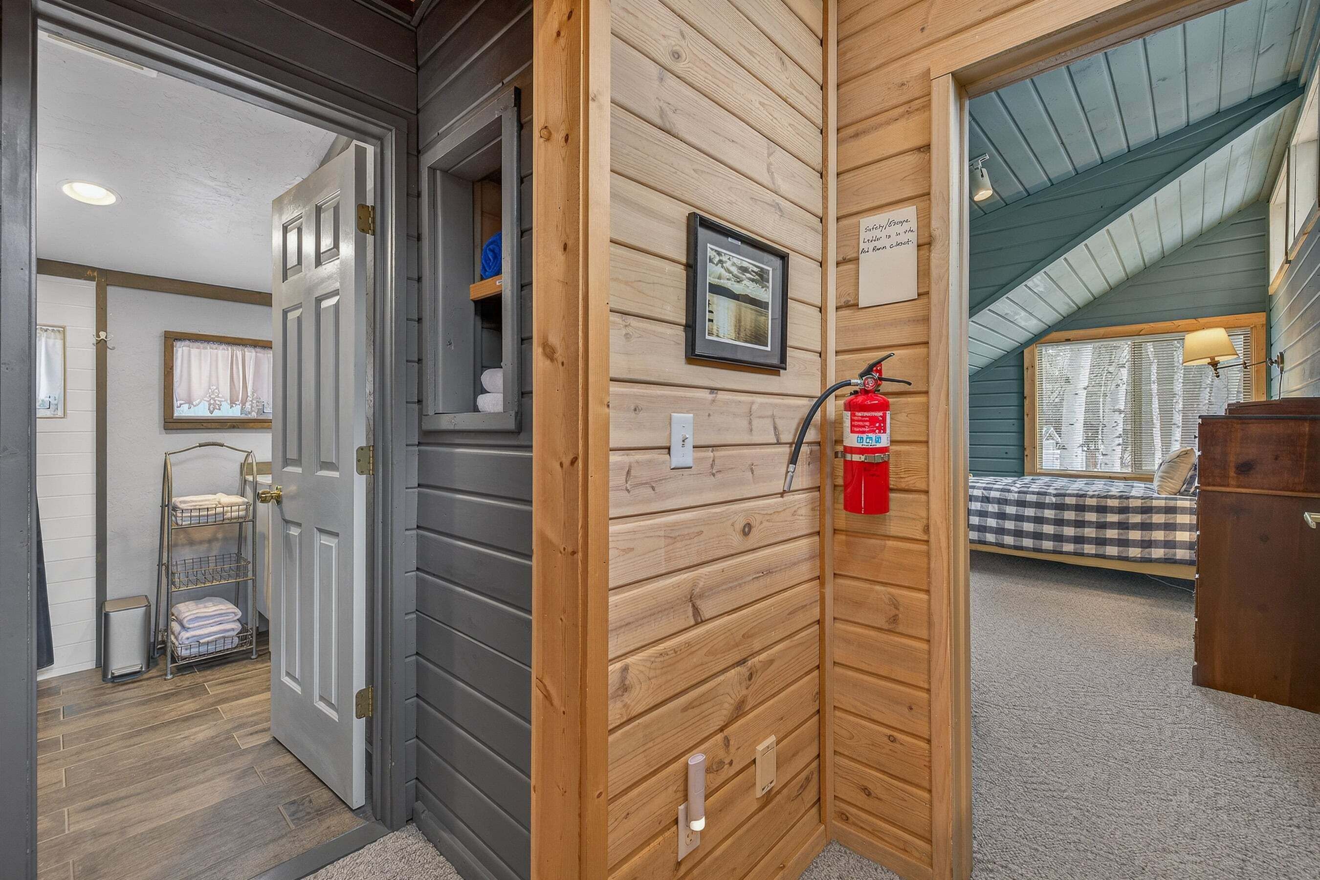A wooden interior with a bed, a fire extinguisher, and a framed picture on the wall.