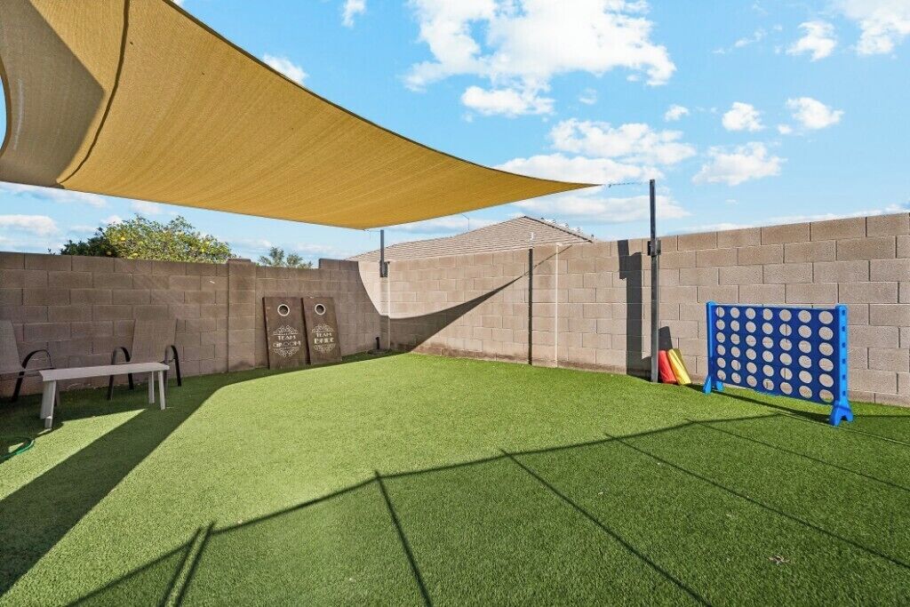 A fenced outdoor area with artificial grass, a bench, and a shaded structure.