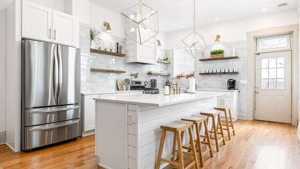 A modern kitchen with a large island, stainless steel appliances, wooden stools, and pendant lighting.
