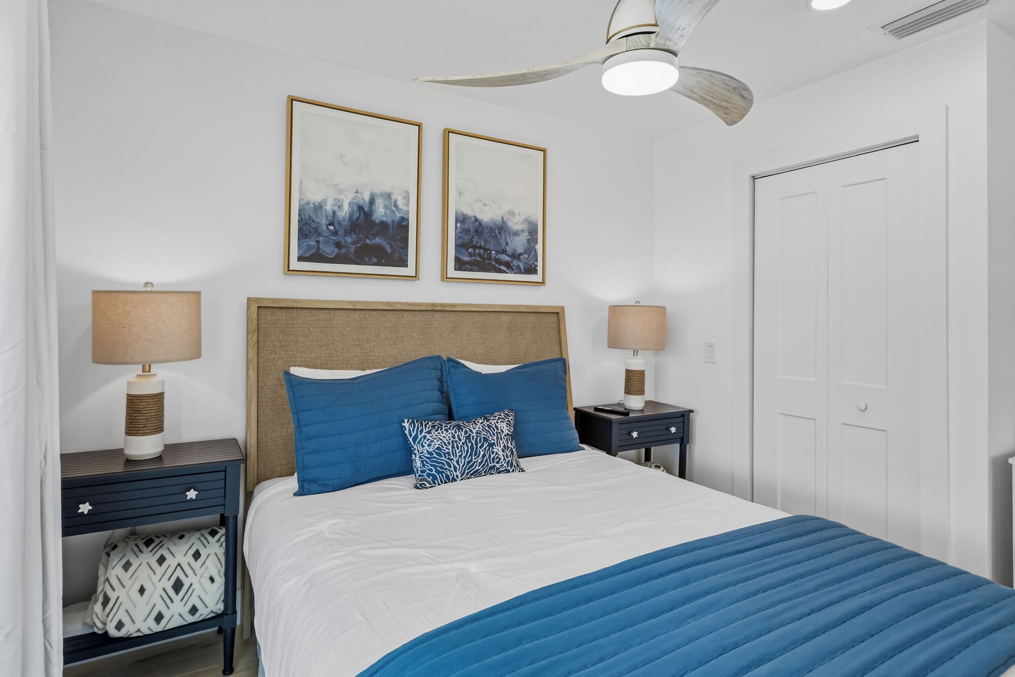 A bedroom with a bed, two bedside tables, a nightstand, a ceiling fan, and two framed pictures on the wall.