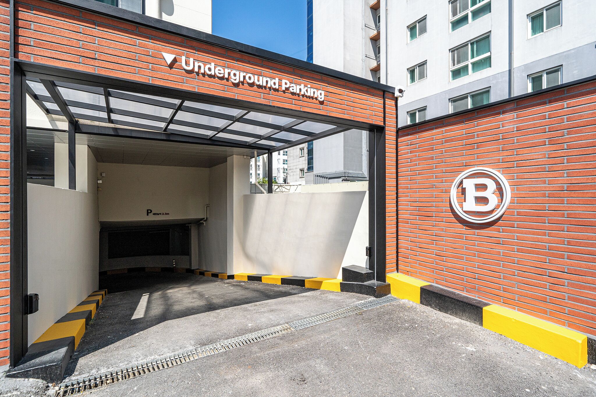 An underground parking entrance with a clear sign, a brick wall, and a yellow curb.