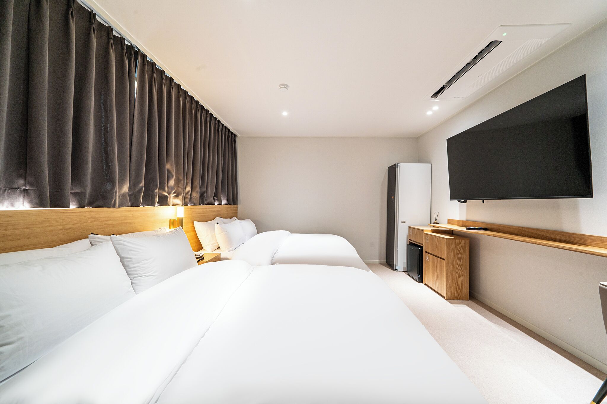 A hotel room with two beds, a flat-screen TV, a wooden nightstand, and a minibar.