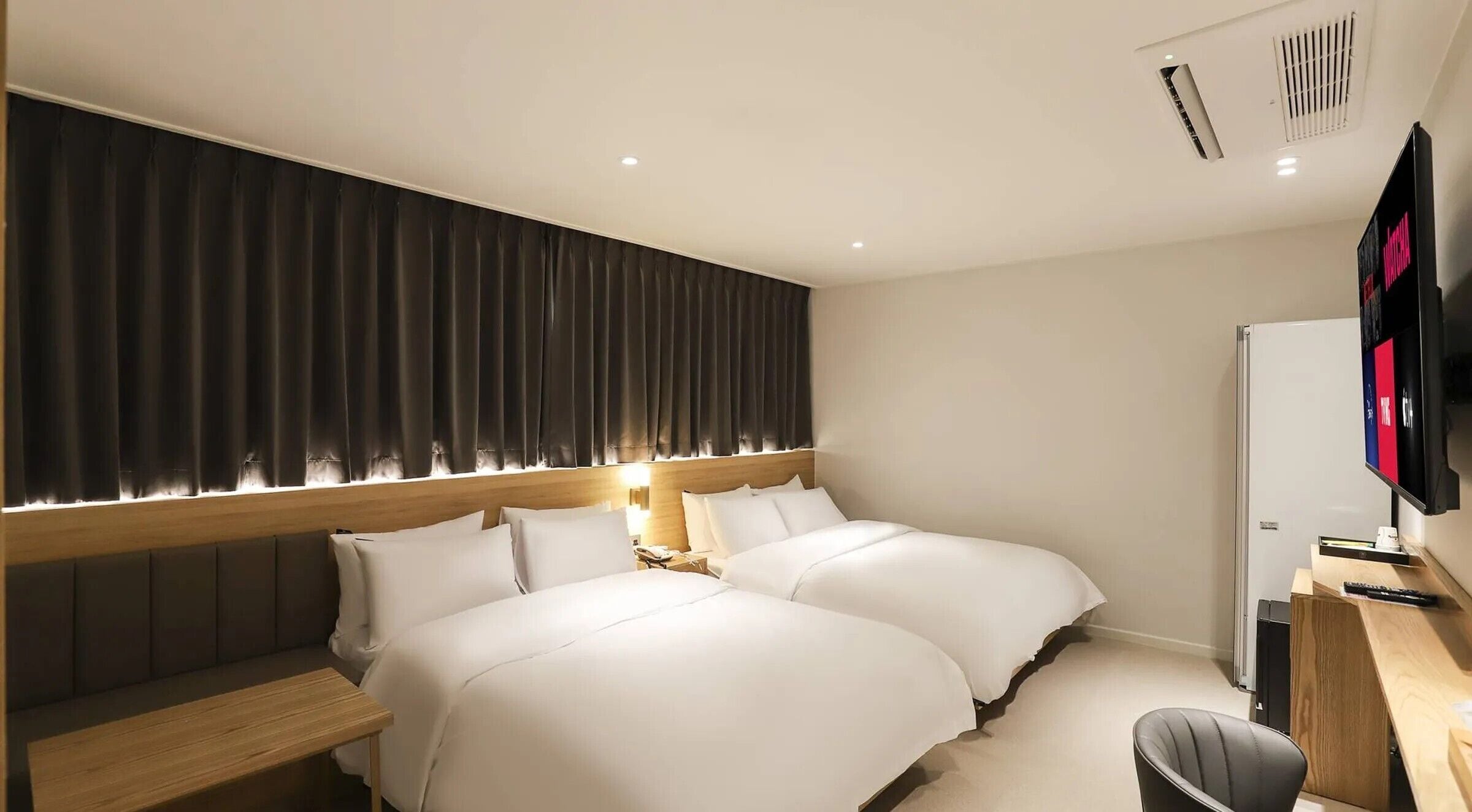 Habitación de hotel con dos camas, un escritorio con computadora, televisión y un ventanal con cortinas.