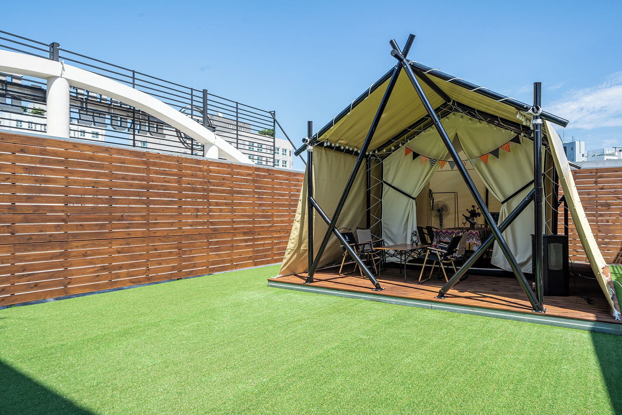 Un espacio al aire libre cubierto con toldo, una cerca de madera, césped artificial y una estructura de metal.