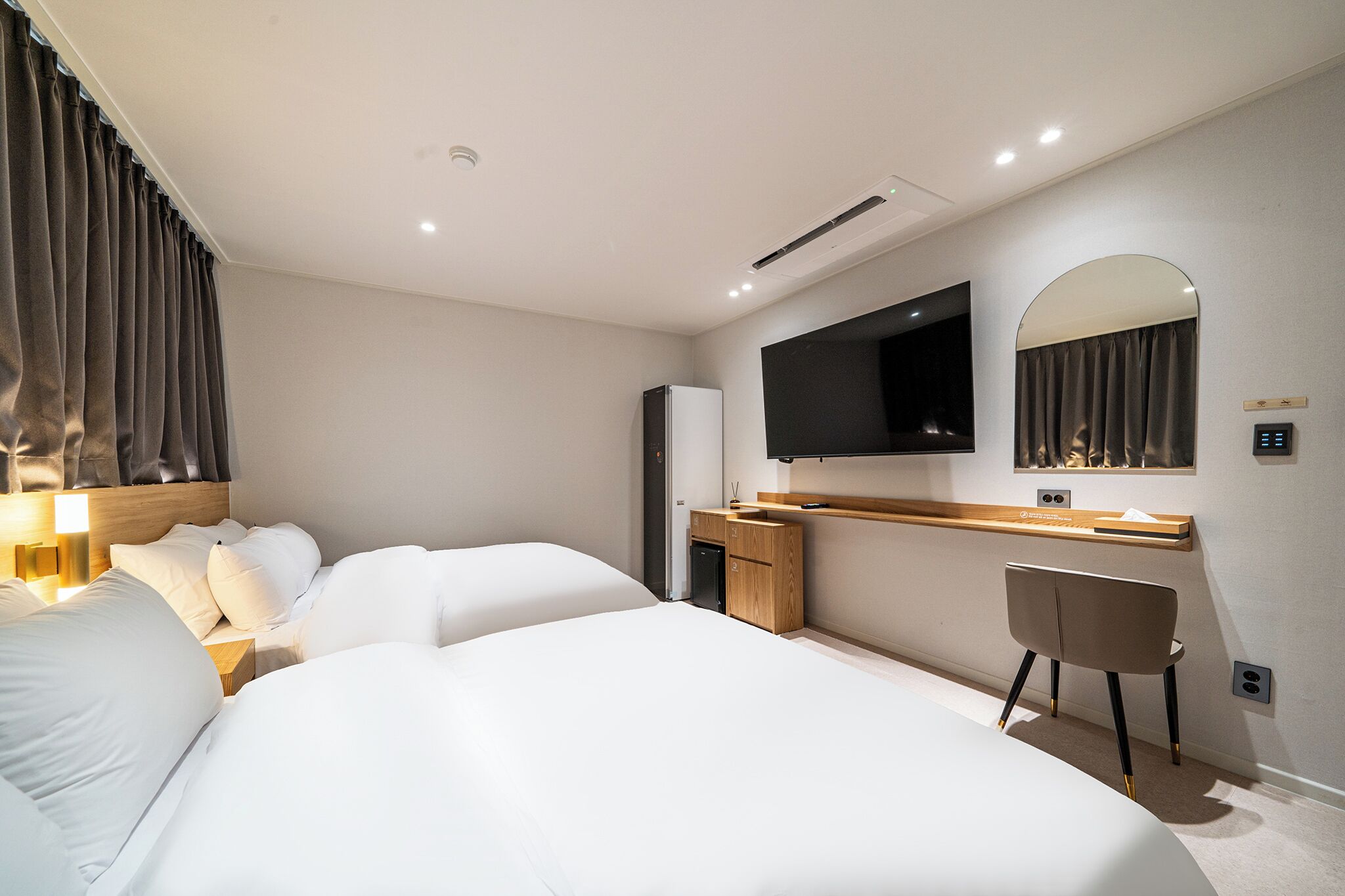 A modern hotel room with a large bed, a desk with a chair, a flat-screen TV, and a mirror on the wall.