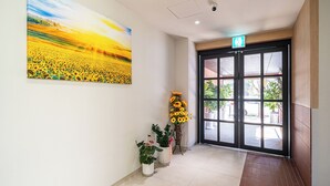A hallway with a large painting of a sunflower field, a potted plant, and a door with a view of the outside. - Brown Dot Hot Spring Yu-Seong (Daejeon)