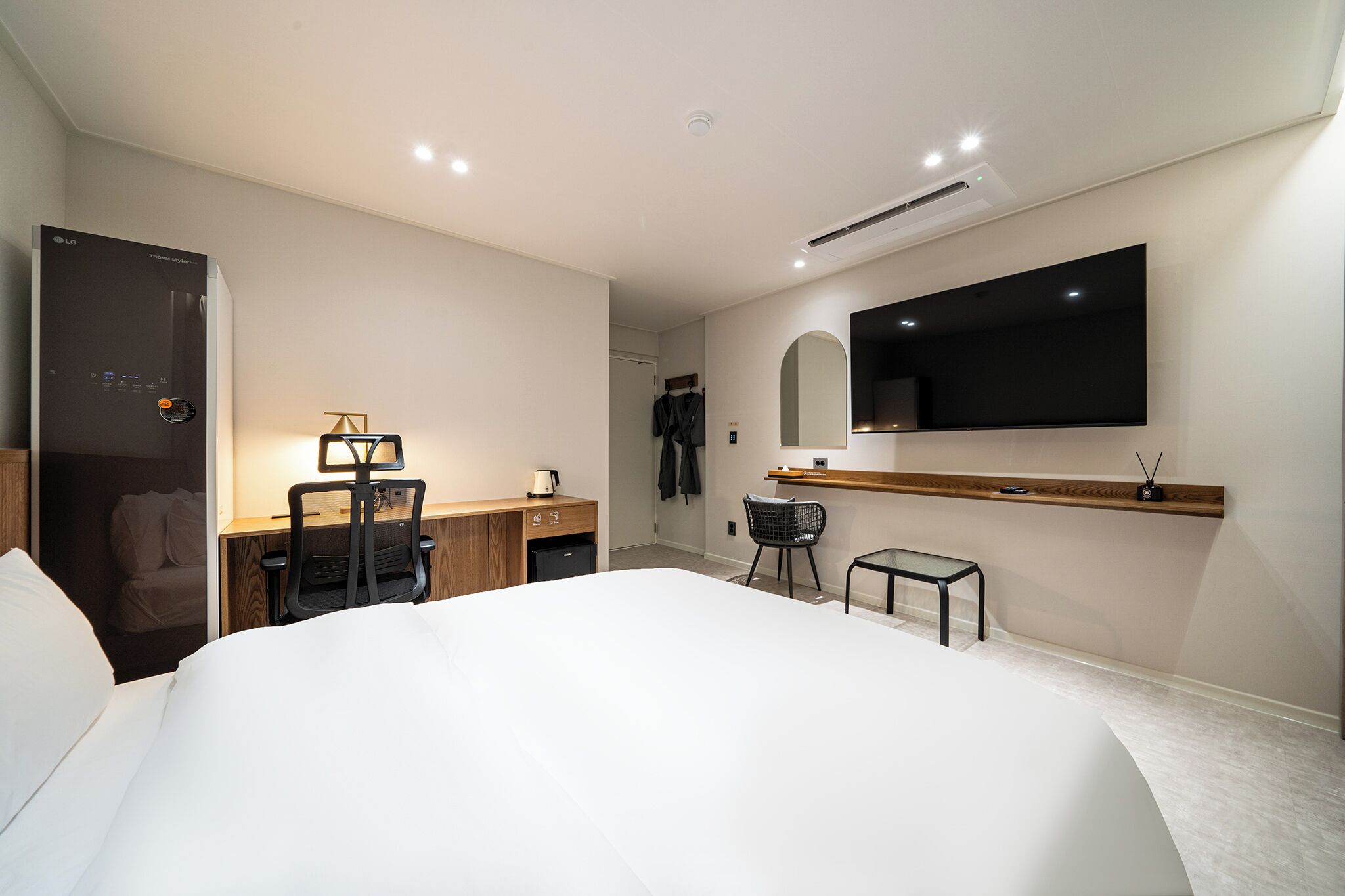 Una habitación de hotel moderna con una cama grande, un escritorio con silla, un televisor montado en la pared y una pequeña mesa con una silla.