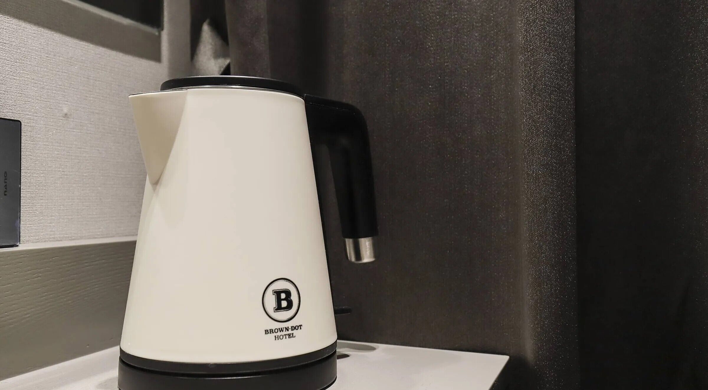 A white electric kettle with a black handle and a logo on the base, placed on a white surface.