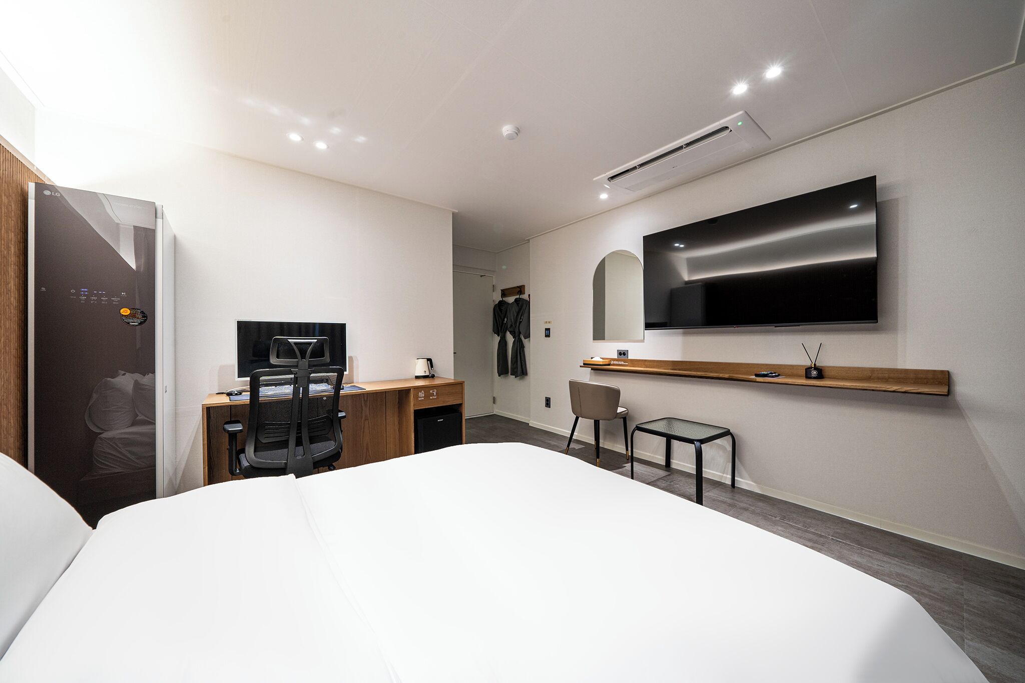 Quarto de hotel moderno com cama, escrivaninha, cadeira, televisão e guarda-roupa.