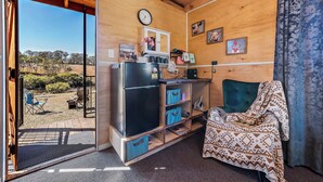 A compact room with a wooden interior, a black refrigerator, a blue chair, and a view of the outdoors. - Glamping @ Undercliff Farm (Undercliffe)
